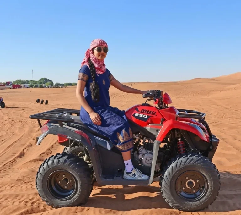 Rider on quad bike crossing Dubai desert dunes under clear sky with golden sand waves showing outdoor adventure travel experience in desert terrainUAE